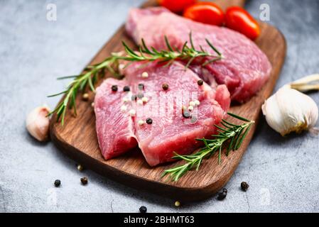 Carne di maiale cruda su tagliere di legno al tavolo da cucina per cucinare bistecca di maiale arrosto o grigliato con ingredienti erbe e spezie, maiale fresco Foto Stock