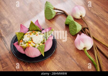 Tradizionale piatto vietnamita: Riso cotto con verdure decorate con foglie di loto e fiori di loto bello su tavola da pranzo in legno Foto Stock