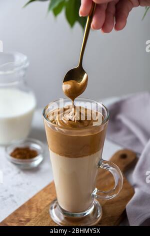 Spalmare la schiuma su un cucchiaio di caffè in algone. Bevanda coreana in un bicchiere alto con caffè montato Foto Stock