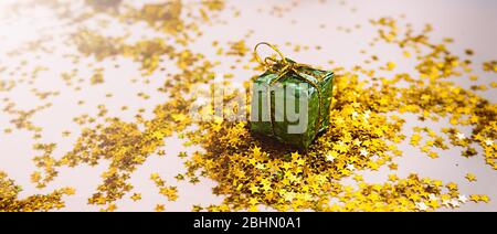 piccolo regalo in lamina verde su sfondo di stelle d'oro sparse su uno sfondo beige morbido. banner di congratulazioni Foto Stock