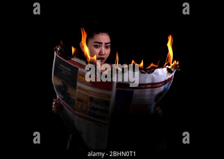 Giovane bella Asia donna è in attesa acceso e legge un fuoco bruciare giornale su sfondo nero, Hot Breaking news concept Foto Stock