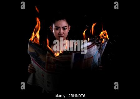 Giovane bella Asia donna è in attesa acceso e legge un fuoco bruciare giornale su sfondo nero, Hot Breaking news concept Foto Stock