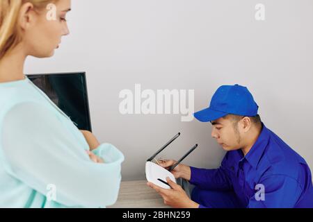 Addetto all'assistenza che installa un router wi-fi dual band in appartamento di una giovane donna Foto Stock