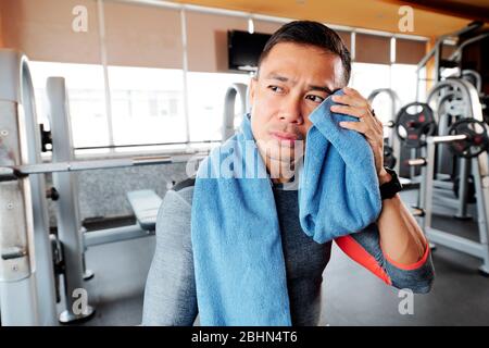 Sportivo stanco che strofinava il sudore dal viso dopo aver sollevato il pesante campanello in palestra Foto Stock