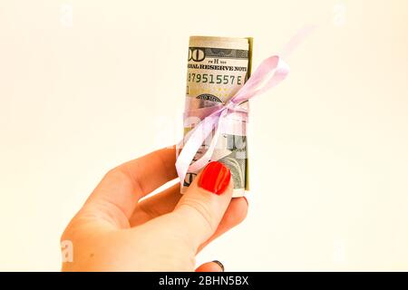 Mano che tiene piccolo regalo del dollaro, pacchetto delle fatture di cento dollari legati con un nastro rosa. Dollari isolati su sfondo bianco Foto Stock