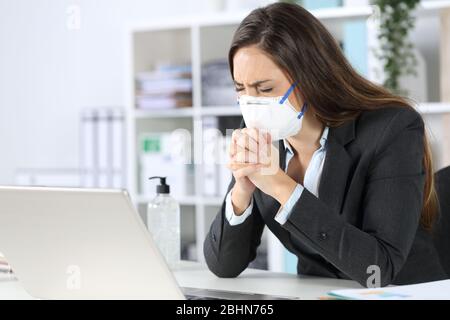 Donna executive che indossa una maschera protettiva che prega con gli occhi chiusi su una scrivania in ufficio Foto Stock