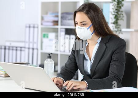 Donna executive che indossa una maschera che lavora su un computer portatile su una scrivania in ufficio Foto Stock