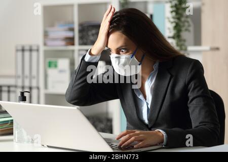 Una donna executive sorpresa con maschera protettiva trova errore sul laptop di notte in ofice Foto Stock