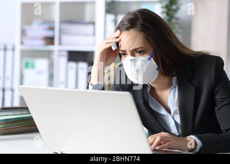 Donna dirigente preoccupata con maschera protettiva che legge le cattive notizie sul laptop in ufficio Foto Stock