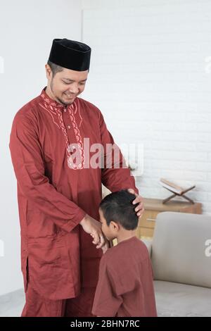 Bambino baciando la mano del padre per scusarsi e dire Happy Eid giorno Foto Stock