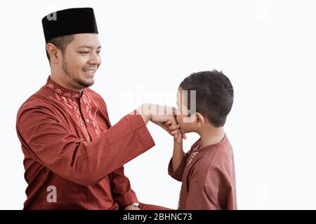 Bambino baciando la mano del padre per scusarsi e dire Happy Eid giorno Foto Stock