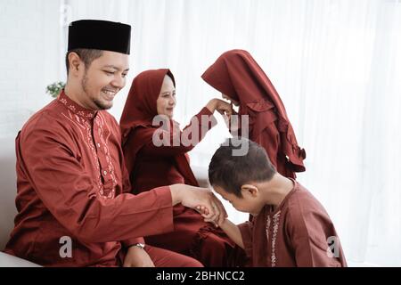 Ragazzo asiatico baciare la mano del padre per scusarsi quando celebra Happy Eid UL-Fitr Foto Stock