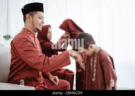 Bambino baciando la mano del padre per scusarsi e dire Happy Eid giorno Foto Stock