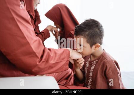 Bambino baciando la mano del padre per scusarsi e dire Happy Eid giorno Foto Stock