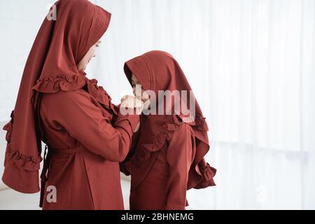 ragazza musulmana asiatica baciare la mano di sua madre per scusarsi quando celebra Happy Eid UL-Fitr Foto Stock