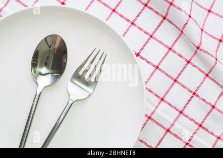 piatto bianco e cucchiaio a forchetta su tovaglia rossa controllata Foto Stock