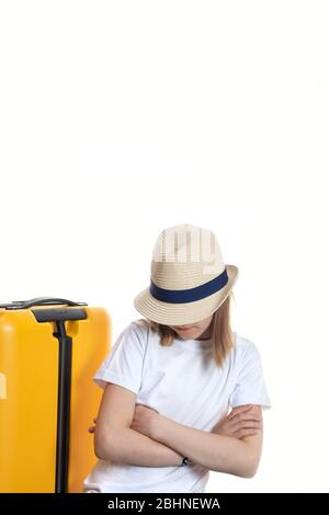 Giovane bella ragazza turistica nascondiglio viso sotto stativi cappello con le mani incrociate sul petto vicino a valigia brillante su ruote. Shot a mezza lunghezza isolato o Foto Stock