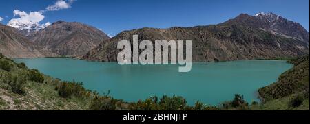 Panorama del verde azzurro lago di Iskanderkul in Tazjikistan con alte montagne innevate. Foto Stock