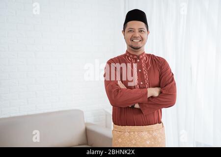 L'uomo asiatico sorride in piedi con le mani incrociate indossando abiti tradizionali malesi Foto Stock