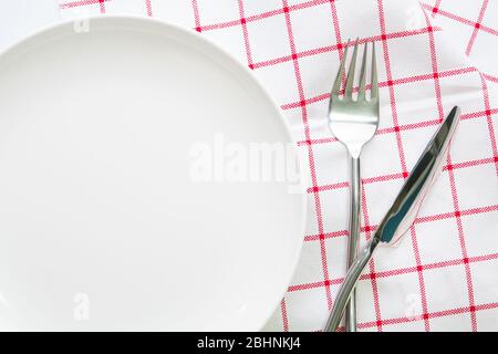 piastra bianca con coltello e cucchiaio a forcella su tovaglia rossa controllata Foto Stock