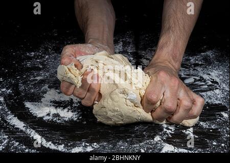 Mani di un uomo che impastano una palla di farina per fare il pane su una superficie nera piena di farina Foto Stock