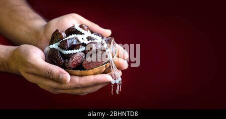 Mano con date isolato sfondo rosso, iftar concetto immagine islamica mani che tengono una ciotola di colore dorato di date con Tasbeeh Foto Stock