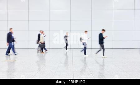 Molti uomini d'affari anonimi stanno camminando attraverso una grande sala luminosa Foto Stock