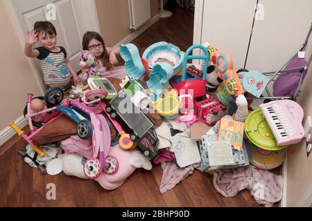 Due fratelli circondati da un enorme mucchio di giocattoli per bambini a casa Foto Stock