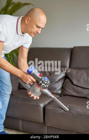 Divano uomo per la pulizia con aspirapolvere manuale mentre lavori nel soggiorno. Servizio di pulizia. Lavori domestici Foto Stock