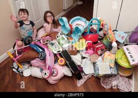 Due fratelli circondati da un enorme mucchio di giocattoli per bambini a casa Foto Stock