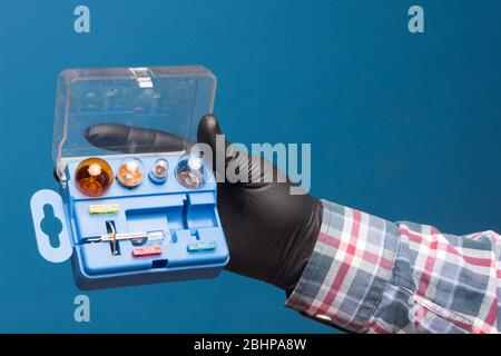 Luci e materiale di ricambio obbligatorio per auto in una scatola di plastica e a portata di mano con guanto nero e sfondo blu Foto Stock