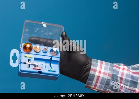 Luci e materiale di ricambio obbligatorio per auto in una scatola di plastica e a portata di mano con guanto nero e sfondo blu Foto Stock