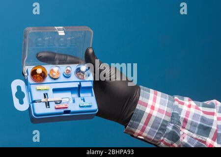 Luci e materiale di ricambio obbligatorio per auto in una scatola di plastica e a portata di mano con guanto nero e sfondo blu Foto Stock