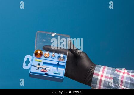 Luci e materiale di ricambio obbligatorio per auto in una scatola di plastica e a portata di mano con guanto nero e sfondo blu Foto Stock