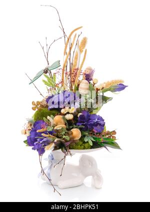 Composizione decorativa pasquale. Un coniglietto contiene una composizione di fiori. Foto Stock