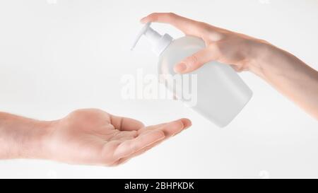 Donna che aiuta la mano dando alcol gel detergente per un uomo. Su sfondo grigio Foto Stock