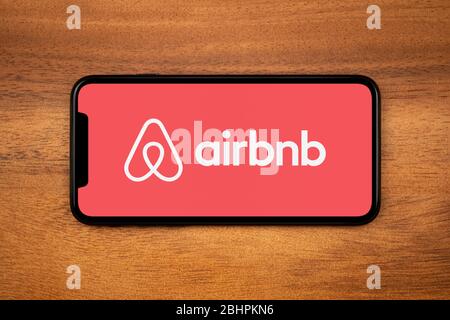 Uno smartphone con il logo Airbnb è appoggiato su un tavolo di legno (solo per uso editoriale). Foto Stock