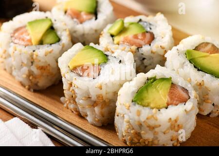 I tradizionali panini di sushi di uramaki di salmone e avocado, rotolati in semi di sesamo, sono serviti su un vassoio di legno da vicino per la pubblicità del menu Foto Stock