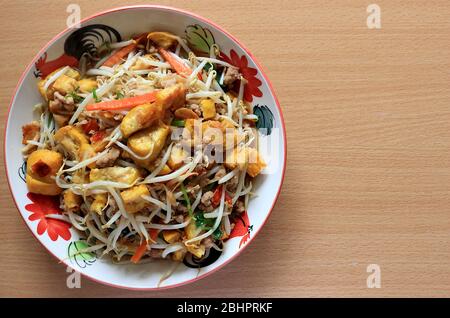 Mescolare i germogli di fagioli fritti con tofu, carote, sedano, maiale macinato, aglio, olio vegetale e un po' di peperoncino. Messo su un piatto su uno sfondo di legno. Foto Stock