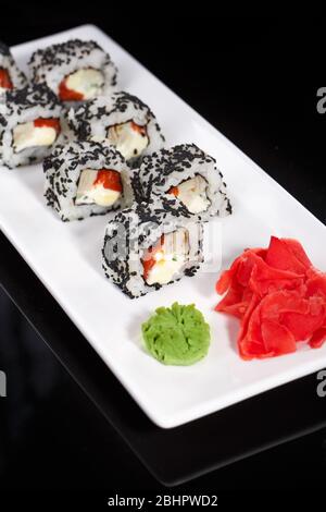 Cucina tradizionale Giapponese. Un rotolo di sushi con sesamo viene servito su un piatto bianco, decorato con wasabi e zenzero. Foto Stock