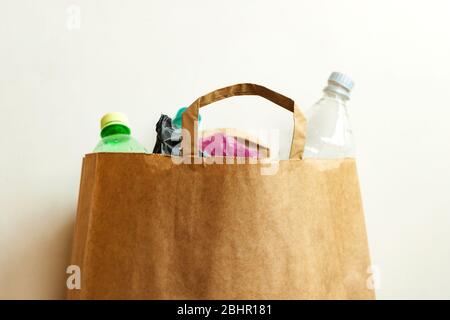 Bottiglie di plastica usate vuote, sacchetti in sacchetti di carta marrone, smistamento dei rifiuti per il riciclaggio su fondo chiaro Foto Stock