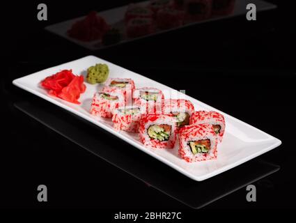 Cucina tradizionale Giapponese. Un rotolo di sushi con caviale è servito su un piatto bianco, decorato con wasabi e zenzero. Foto Stock