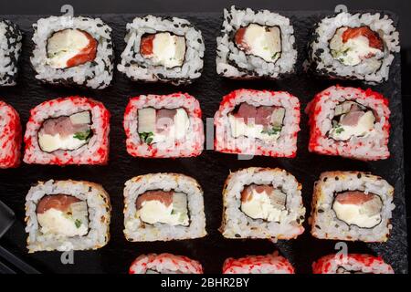 Sushi roll cibo giapponese nel ristorante. Diversi tipi di sushi roll set con salmone, verdure, pesce, caviale e sesamo su sfondo nero. Foto Stock