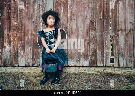 Una ragazza vestita come una strega per Halloween in piedi di fronte ad una recinzione. Foto Stock