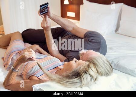 Una coppia sdraiata su un letto che porta un selfie su un telefono cellulare. Foto Stock