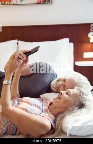 Una coppia sdraiata su un letto che guarda un telefono cellulare. Foto Stock