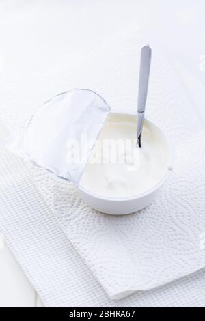 Yogurt greco semplice in tazza con cucchiaio su sfondo bianco Foto Stock