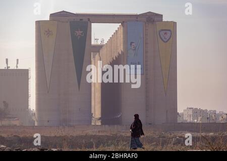 Una donna locale e i silos di grano di Hasakah sullo sfondo all'alba, Siria. Foto Stock