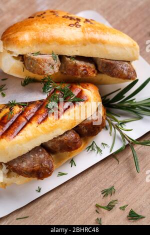 Arrossire i sandwich con salsicce, aneto e un filo di basilico su un piatto bianco su un tavolo di legno. L'idea di cottura veloce. Foto Stock