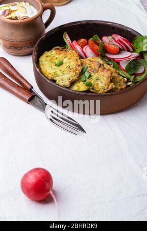 Frittelle di zucchine, piatto vegetariano con zucchine appena grattugiate, tuorlo d'uovo, pistacchi e cipolla in rustica ciotola di ceramica servita con insalata verde, Foto Stock